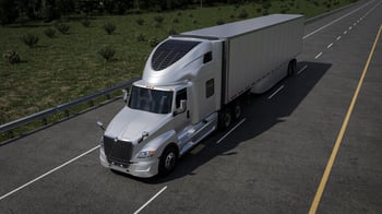 Silver International LT semi-truck with a fairing integrated solar panel with a long box trailer driving on a multi-lane highway bordered by grass and trees.