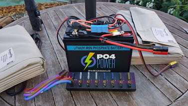 Lithium iron phosphate battery with an Anderson Powerpole strip and two 60W Foldable Solar Panels on a circular wooden table