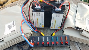 Lithium iron phosphate battery with two Genasun charge controller moundted on the back with an Anderson Powerpole strip and two 60W Foldable Solar Panels on a circular wooden table.jpg