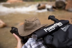 A photographer crouching down to take a photo with a rolled up LightSaver Max Portable Solar Charger on his back