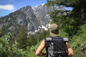 Hiker staring at the mountains in the distance with a LightSaver Portable Solar Charger on his back