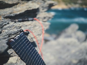 LightSaver Portable Solar Charger unrolled on a rock edge charging a cell phone