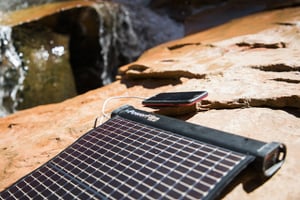 Unrolled LightSaver Max Portable Solar Charger on a rock charging a cell phone