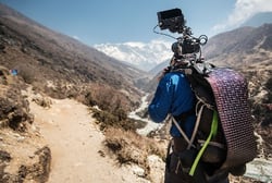 Videographer hiking with his camera and a LightSaver Max Portable Solar Charger unrolled on his backpack