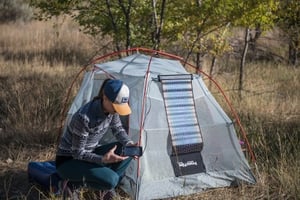 Woman charging her cell phone via the LightSaver Max Portable Solar Charger unrolled on a on a tent