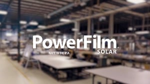 PowerFilm white logo on top of blurred background of PowerFilm manufacturing facility