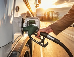 Hand holding fuel pump nozzle, refueling RV at sunset. Golden light illuminates trees and road in background