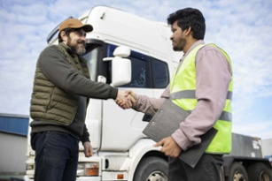 Truck driver shaking hands with logistics worker in safety vest. White truck in background. Professional interaction at job site.