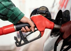 Close-up of a person refueling a vehicle with a red gasoline nozzle at a gas station