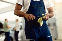 Mechanic in a blue uniform holding a wrench and cloth in a service workshop with people in the background