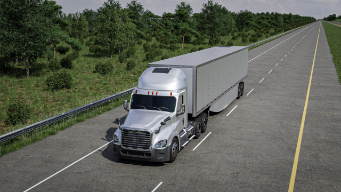 A silver semi-truck with a trailer drives on a long, straight road bordered by green trees with a solar panel on the fairing.