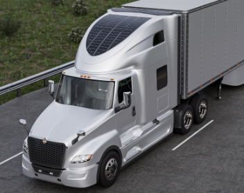 Silver commercial semi-truck with solar panels mounted on the roof of the cab, driving on a road with grass along the side.