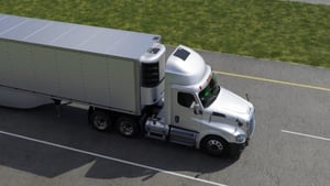 Large commercial refrigerated delivery truck with silver exterior and gray cargo container, traveling on a paved road