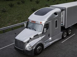 Silver semi-truck with a trailer parked on the road, featuring a solar panel installed on the roof of the cab.