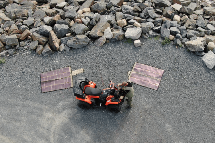Lightweight solar charging panels deployed beside a motorcycle during a remote amateur radio field operation.
