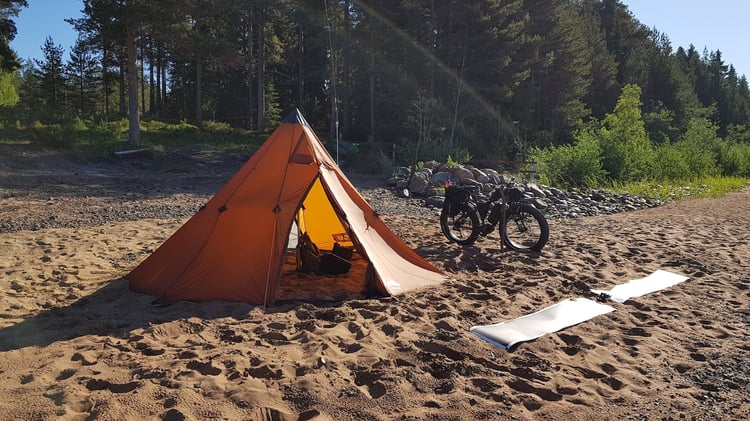 Portable amateur radio station deployed from an electric fat bike with a shelter tent and rollable solar panels on a sandy shoreline.